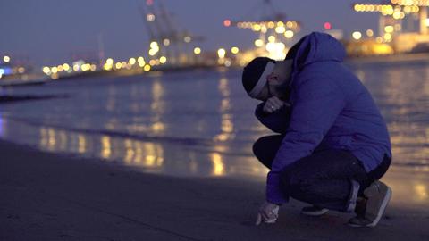 Der Protagonist Danisch hockt niedergeschlagen am Elbstrand. Im Hintergrund sind die Lichter vom Hafen zu erkennen.