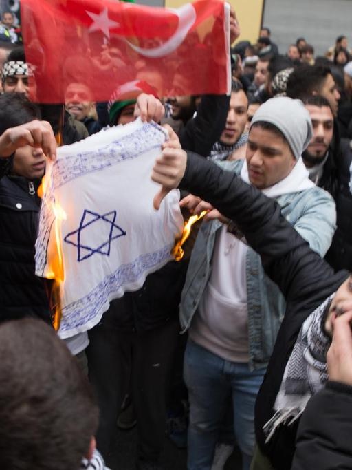 Teilnehmer einer Demonstration verbrennen am 10.12.2017 eine selbstgemalte Fahne mit einem Davidstern in Berlin im Stadtteil Neukölln.