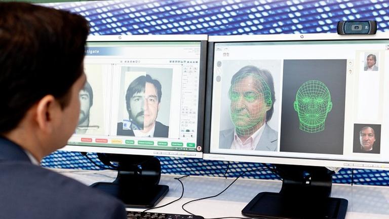 Ein Mann sitzt vor einem Computerbildschirm und arbeitet mit einem automatischen Gesichtserkennungssystem. Ein Mann sitzt vor einem Computerbildschirm und arbeitet mit einem automatischen Gesichtserkennungssystem.