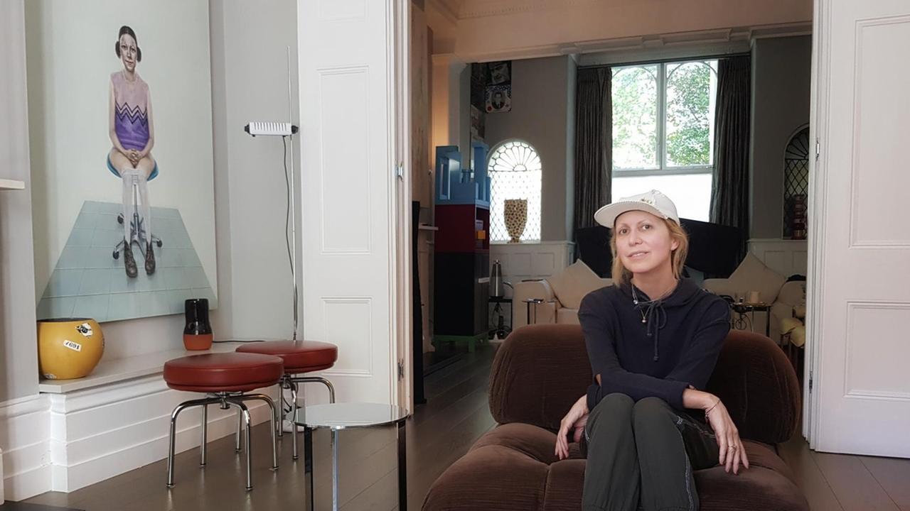 Die Kunstsammlerin Valeria Napoleone sitzt auf einem Sessel und blickt in die Kamera. Links von ihr ist ein Gemälde oder ein bearbeitetes Foto an der Wand. Darauf ist eine junge Frau zu sehen, die auf einem Bürostuhl sitzt. Ihre Strumpfhose ist bis zu den Knien heruntergezogen. Die Kunstsammlerin Valeria Napoleone sitzt auf einem Sessel und blickt in die Kamera. Links von ihr ist ein Gemälde oder ein bearbeitetes Foto an der Wand. Darauf ist eine junge Frau zu sehen, die auf einem Bürostuhl sitzt. Ihre Strumpfhose ist bis zu den Knien heruntergezogen.