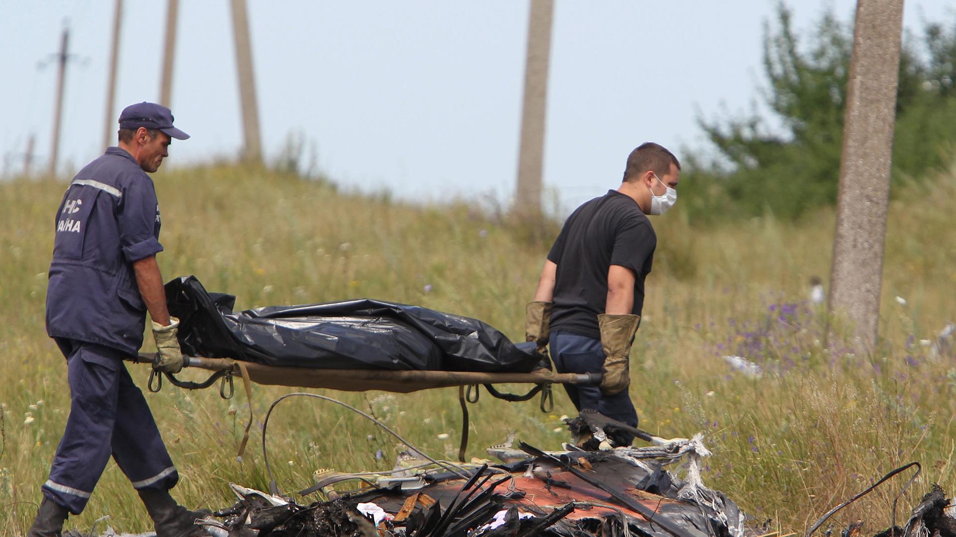 Hinter Trümmern tragen zwei ukrainische Arbeiter eine Bahre, auf der ein abgedecktes Todesopfer liegt. Hinter Trümmern tragen zwei ukrainische Arbeiter eine Bahre, auf der ein abgedecktes Todesopfer liegt.