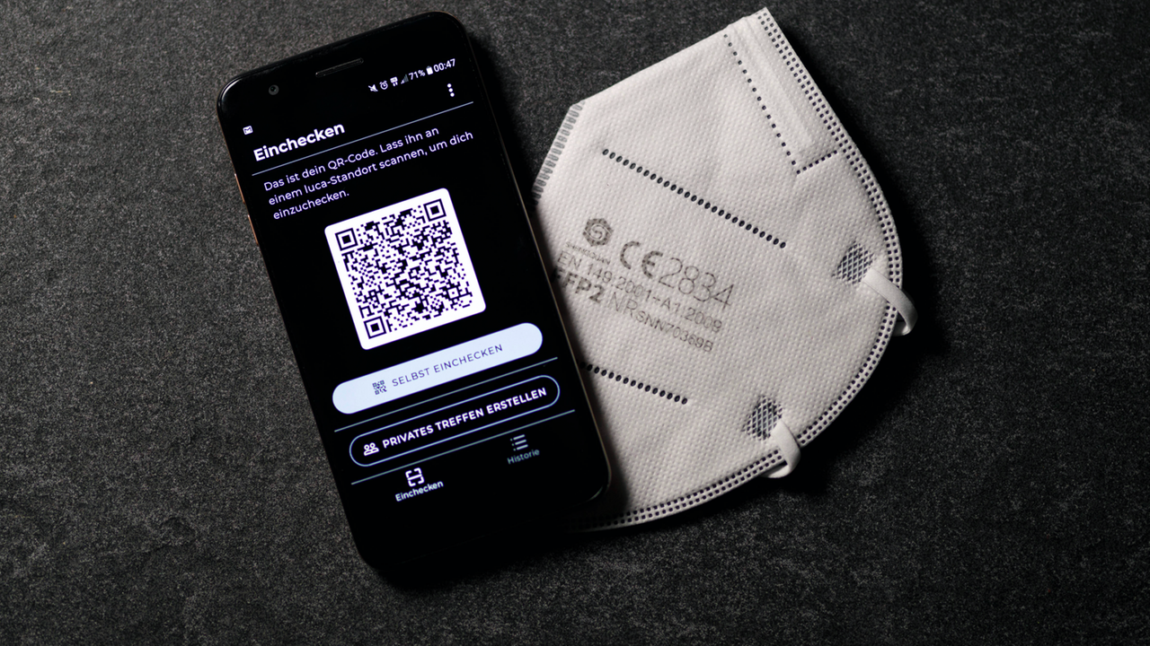 Auf einem Smartphone wird die Check-In-app Luca angezeigt, daneben liegt ein FFP2- Mundschutz Auf einem Smartphone wird die Check-In-app Luca angezeigt, daneben liegt ein FFP2- Mundschutz
