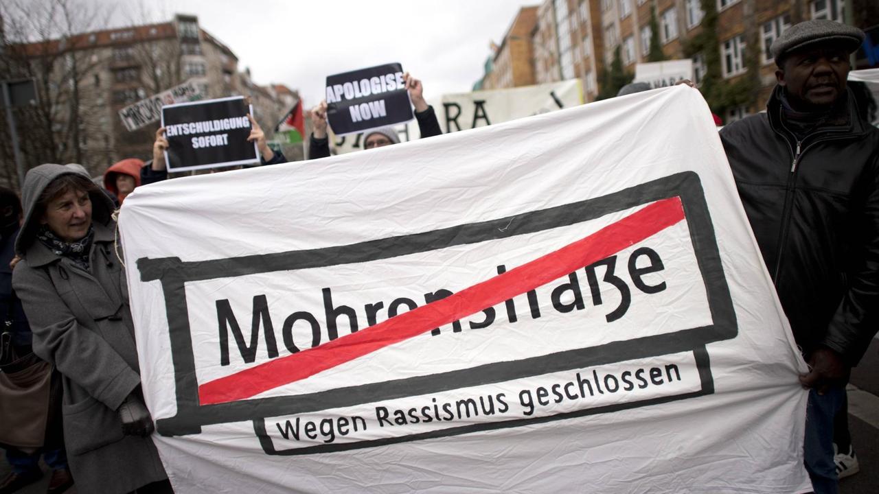 Demonstranten halten ein Transparent mit dem Straßenschild "Mohrenstraße", das rot durchgestrichen wurde. 