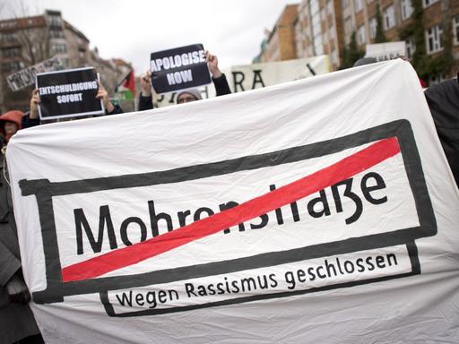 Demonstranten halten ein Transparent mit dem Straßenschild "Mohrenstraße", das rot durchgestrichen wurde.