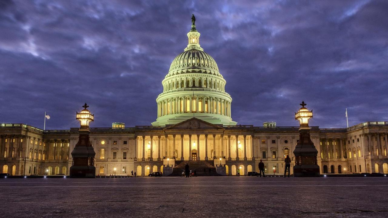 Das Bild zeigt das Kapitol in Washington, es dämmert gerade vor einem bewölkten Himmel. Im Gebäude sind viele Lichter eingeschaltet.