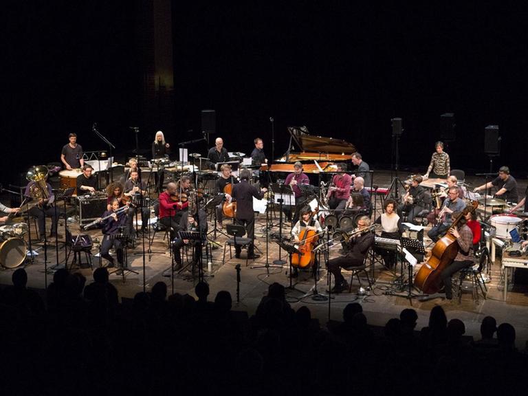 Viele Musiker sitzen in einem breiten Lichtkegel