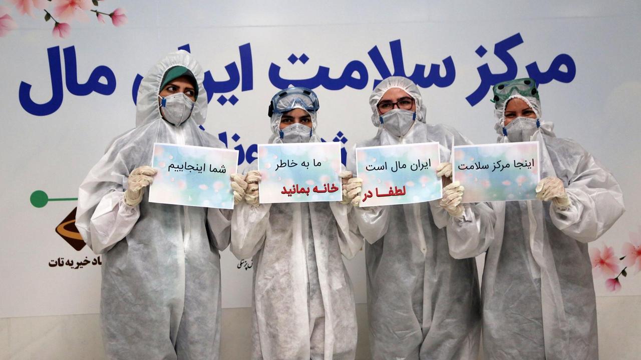 Vier Menschen aus der Krankenpflege in Schutzanzügen halten Schilder hoch: "Bitte bleibt zu Hause! Wir sind für Euch da!" 21.März, Teheran, Iran. Vier Menschen aus der Krankenpflege in Schutzanzügen halten Schilder hoch: "Bitte bleibt zu Hause! Wir sind für Euch da!" 21.März, Teheran, Iran.