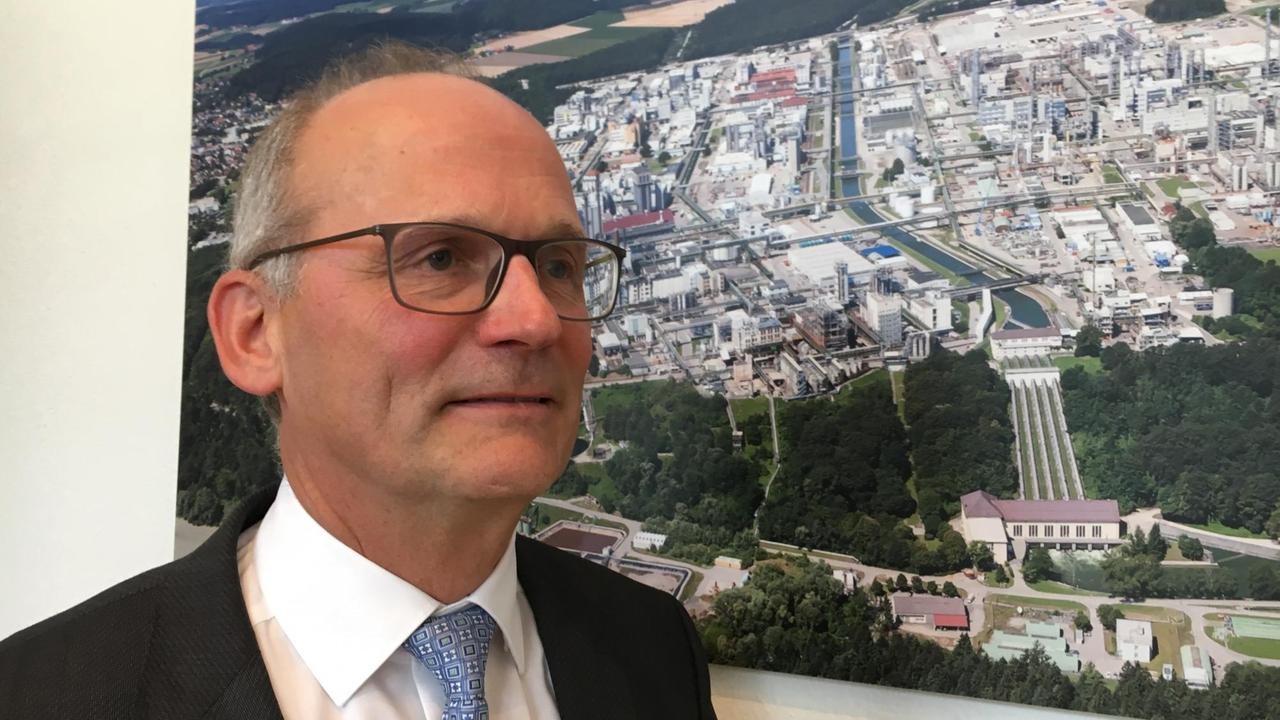 Porträtaufnahme von Dieter Gilles vor einem Foto des Wacker-Werkes. Porträtaufnahme von Dieter Gilles vor einem Foto des Wacker-Werkes.