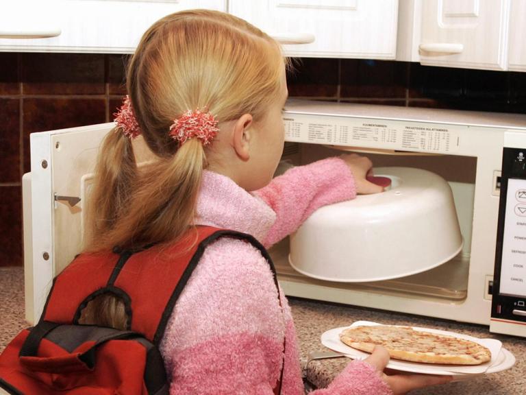 Ein junges Mädchen, das gerade von der Schule nach Haus gekommen ist, wärmt sich in der Mikrowelle etwas zu Essen auf, aufgenommen am 23.11.2004 in Espoo in Finnland.