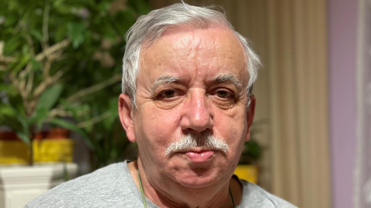 Ein älterer Mann mit Schnurrbart sitzt in einem Zimmer. Ein älterer Mann mit Schnurrbart sitzt in einem Zimmer.
