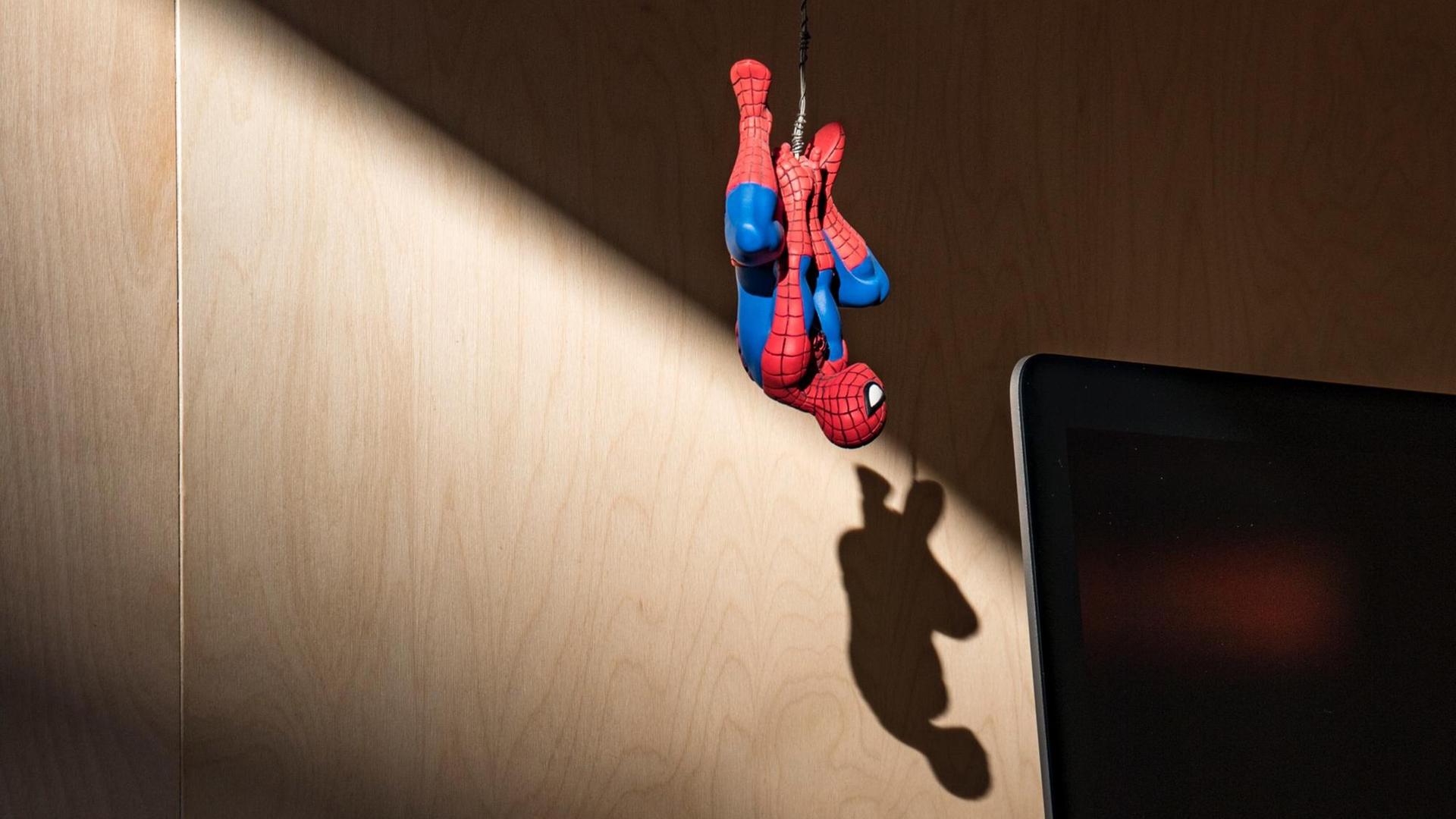 Eine Spiderman-Spielfigur hängt kopfüber vor einem Monitor. Eine Spiderman-Spielfigur hängt kopfüber vor einem Monitor.