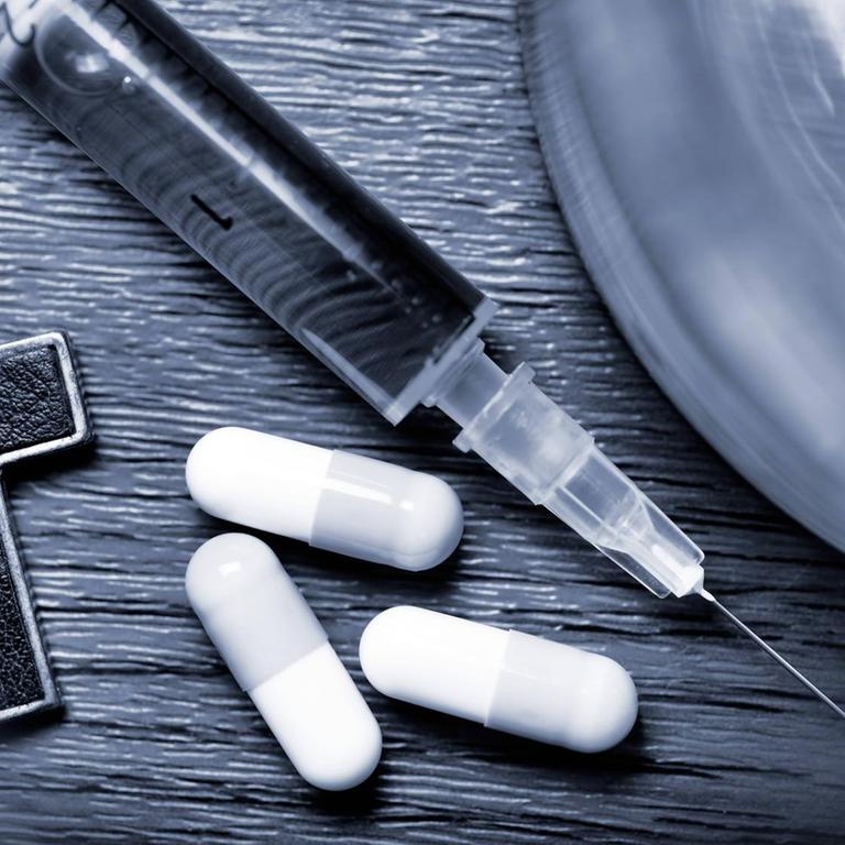 Wasserglas, Kreuz, Tabletten und Spritze auf einem schwarz-weißen Foto.