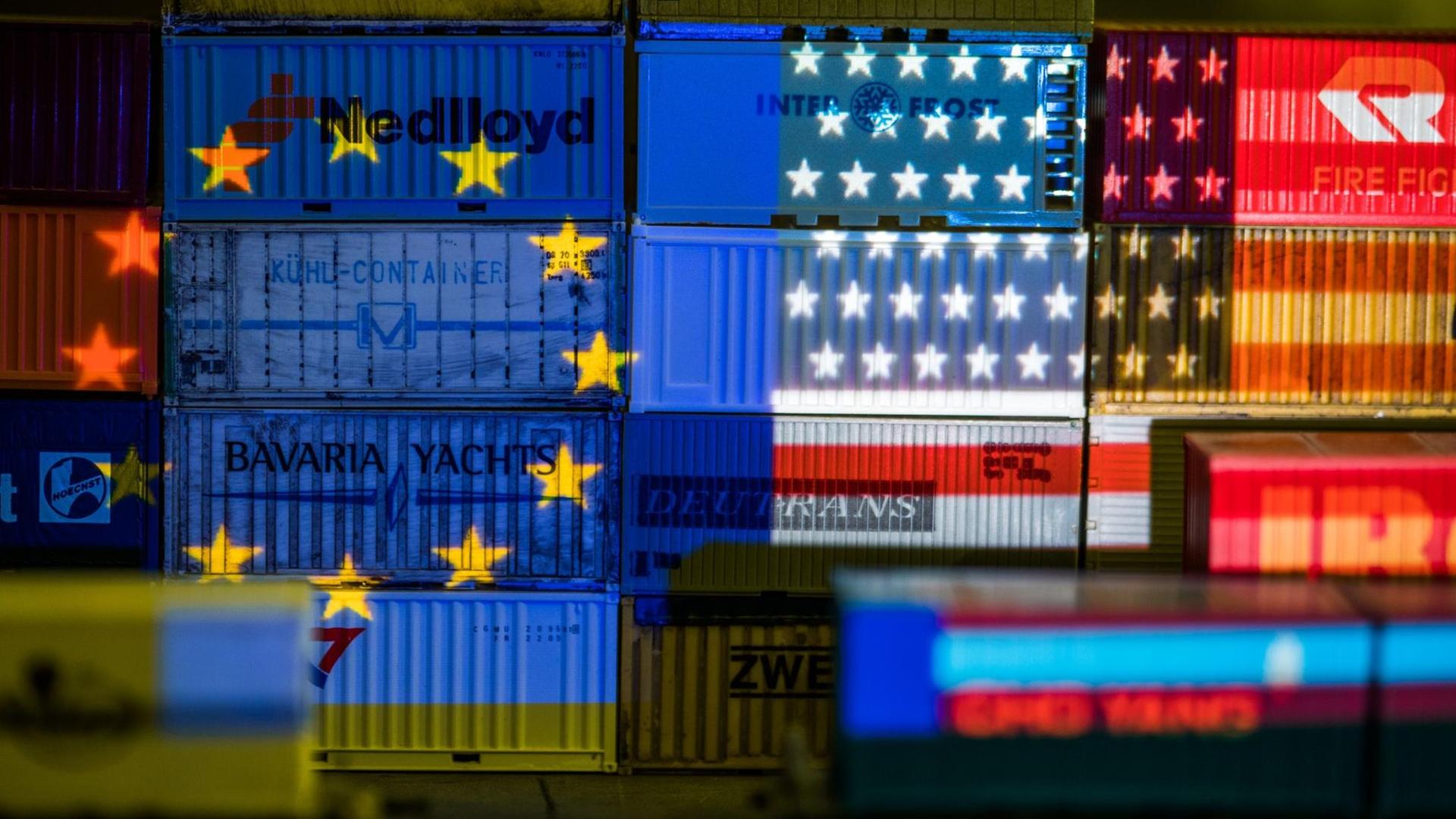 Die Flaggen von Europa und den USA werden mit einem Beamer auf Container projiziert.