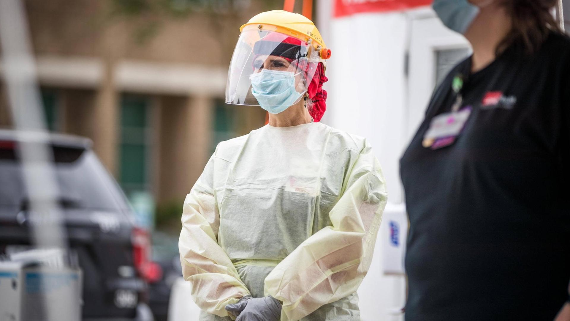 Eine Frau mit Schutzkleidung, Plexiglasmaske und gelbem Helm steht auf der Straße. Eine Frau mit Schutzkleidung, Plexiglasmaske und gelbem Helm steht auf der Straße.