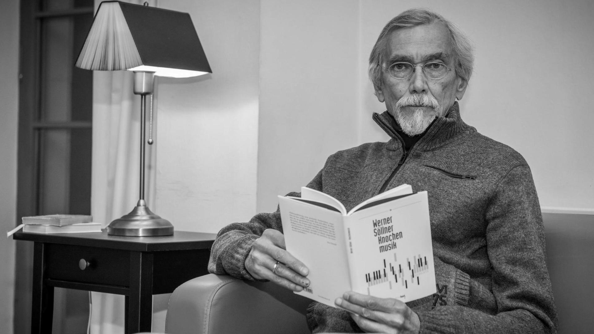 Der Lyriker Werner Söllner auf einem Sofa mit einem Buch. (s-w)