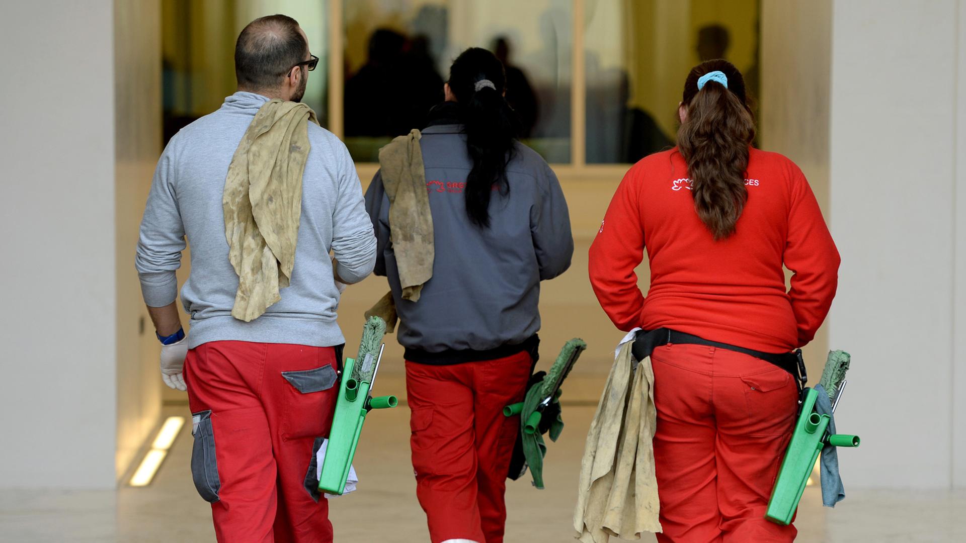 Gebäudereiniger laufen mit ihren Arbeitsmaterialien am Gürtel in ein Gebäude. Gebäudereiniger laufen mit ihren Arbeitsmaterialien am Gürtel in ein Gebäude.