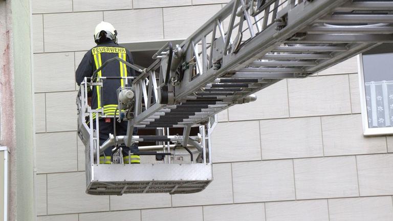 Ein Feuerwehrmann auf einer Hebebühne vor einem Wohnhaus. Ein Feuerwehrmann auf einer Hebebühne vor einem Wohnhaus.