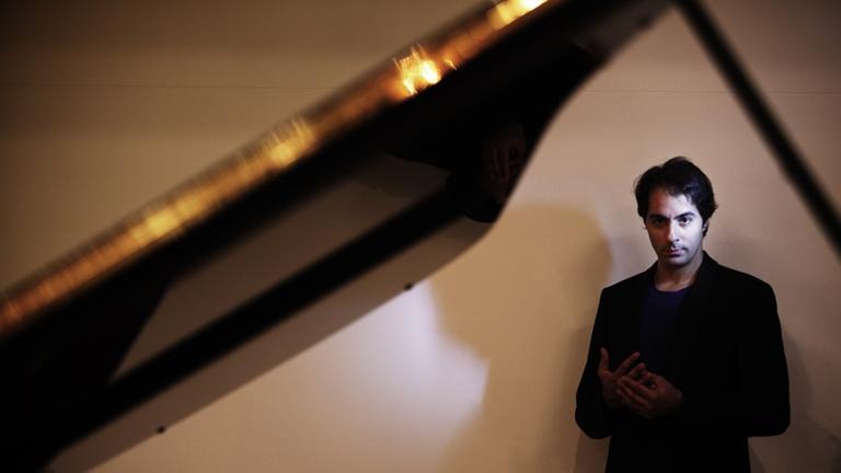 Der Pianist Saleem Ashkar steht in schwarzem Blazer hinter einem aufgeklappten Flügel. Der Pianist Saleem Ashkar steht in schwarzem Blazer hinter einem aufgeklappten Flügel.