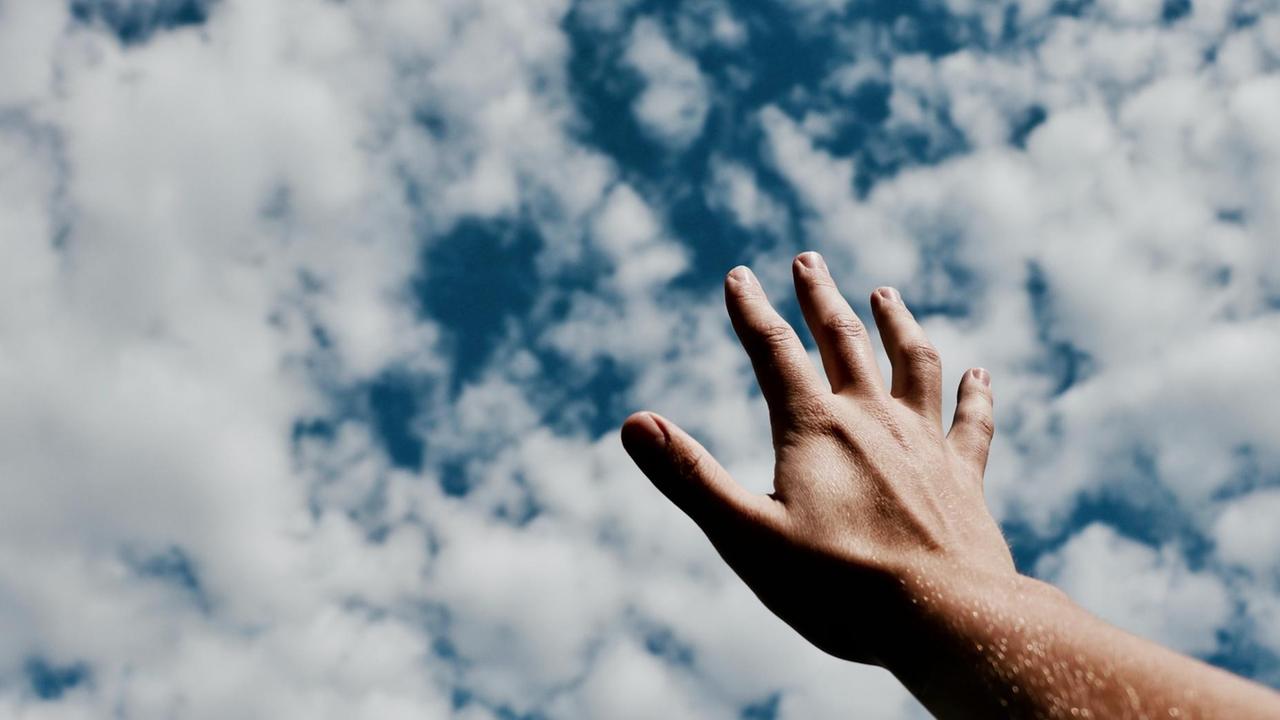 Eine Hand streckt sich dem blauen Himmel mit Schäfchenwölkchen entgegen.