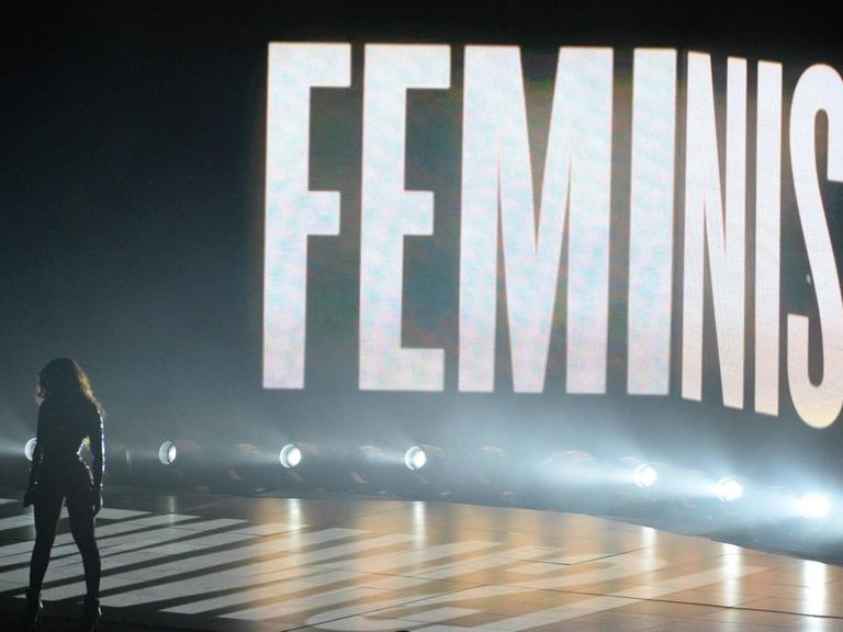 Beyoncé auf der Bühne, das Wort "FEMINIST" leuchtet in weissen Versalien auf der Bühnenwand.