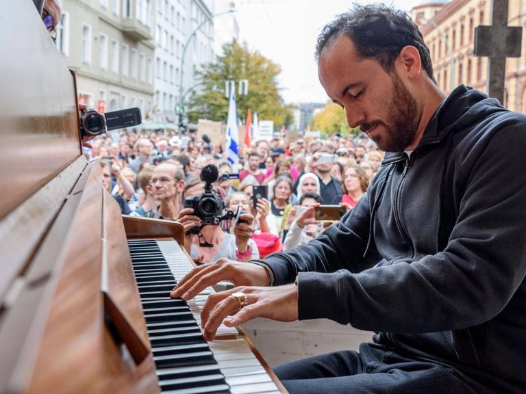 Pianist Igor Levit am Klavier im Freien vor einer Menschenmenge in einer Häuserschlucht.