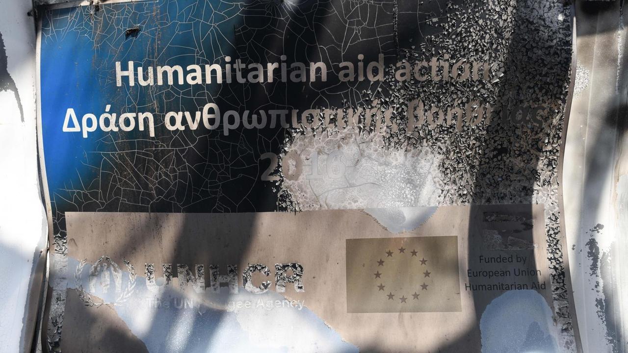 Ein verbranntes Schild "Humanitarian aid action" nach dem Brand im Flüchtlingslager auf Lesbos im September 2015. Ein verbranntes Schild "Humanitarian aid action" nach dem Brand im Flüchtlingslager auf Lesbos im September 2015.