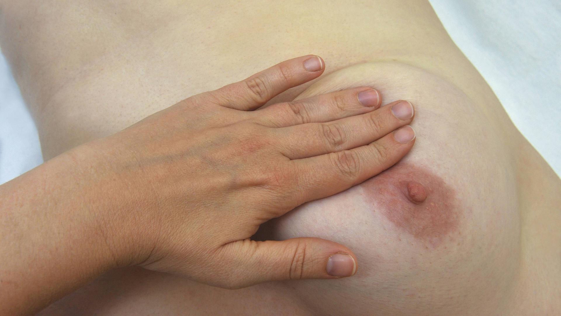 Eine Frau liegt auf dem Rücken und tastet ihre Brust nach Knötchen ab. Eine Frau liegt auf dem Rücken und tastet ihre Brust nach Knötchen ab.