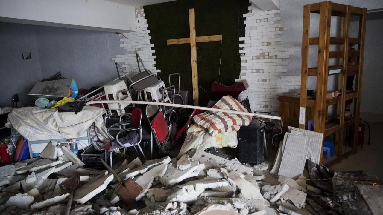Ein Holzkreuz ragt in einer kleinen Familienkirche aus Trümmerteilen hervor. Ein Holzkreuz ragt in einer kleinen Familienkirche aus Trümmerteilen hervor.