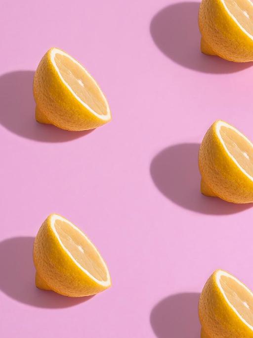 Aufgeschnittene Zitronenhälften liegen auf pinkem Untergrund.