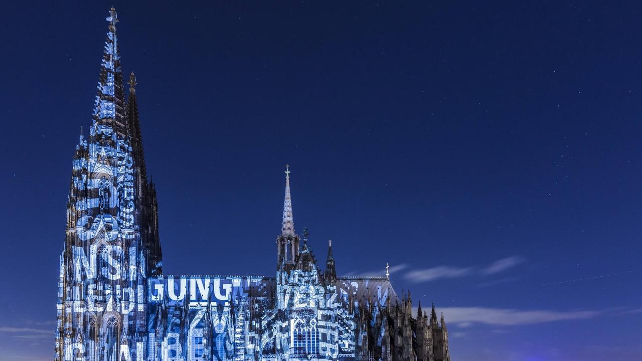 Eine Lichtinstallation der lit. Cologne taucht den Kölner Dom in blaues Licht und projiziert Worte auf die Außenwand.