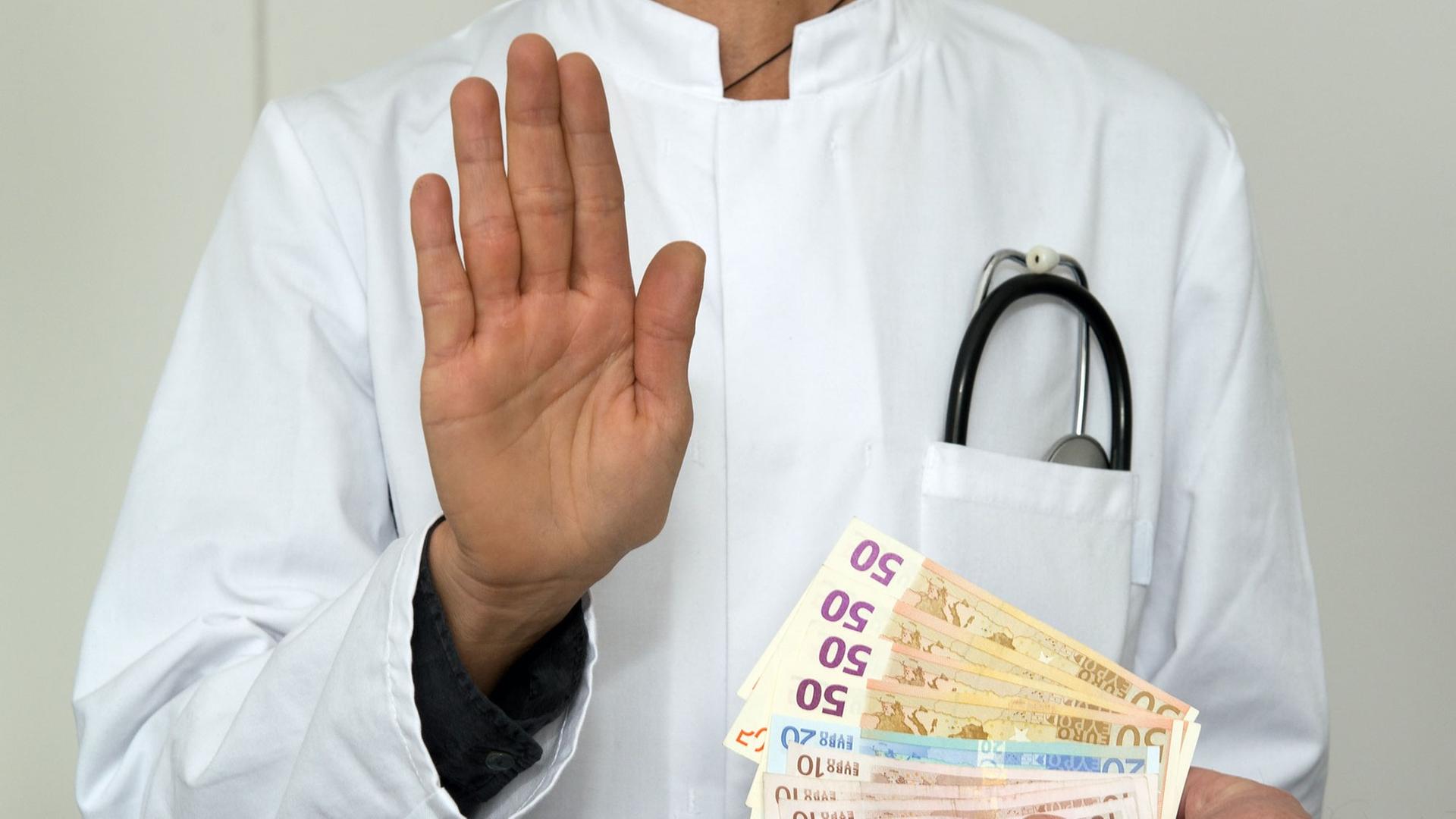 Ein Mann im Arztkittel mit Geldscheinen. Das Symbolfoto steht für Medizin, Geld, Finanzen, Bestechlichkeit, Korruption Ein Mann im Arztkittel mit Geldscheinen. Das Symbolfoto steht für Medizin, Geld, Finanzen, Bestechlichkeit, Korruption