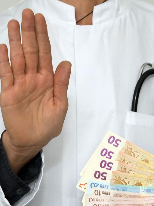 Ein Mann im Arztkittel mit Geldscheinen. Das Symbolfoto steht für Medizin, Geld, Finanzen, Bestechlichkeit, Korruption