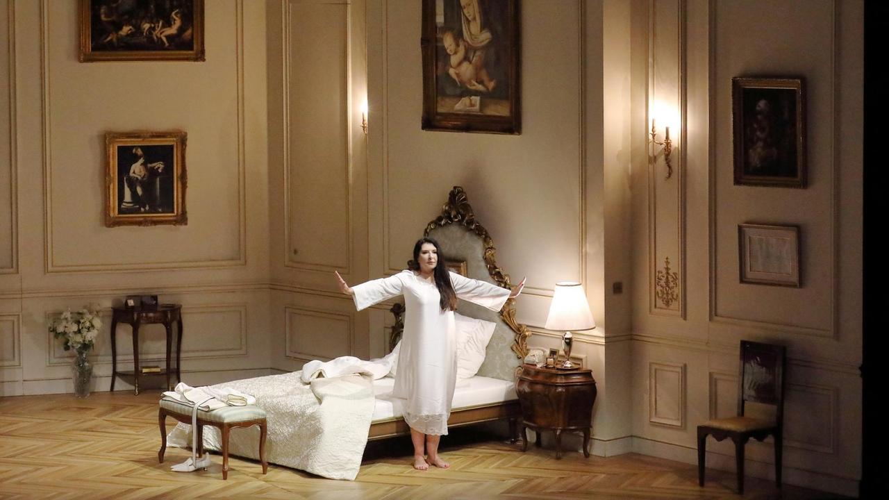 Eine Frau in einem weißen Kleid steht vor einem Bett.