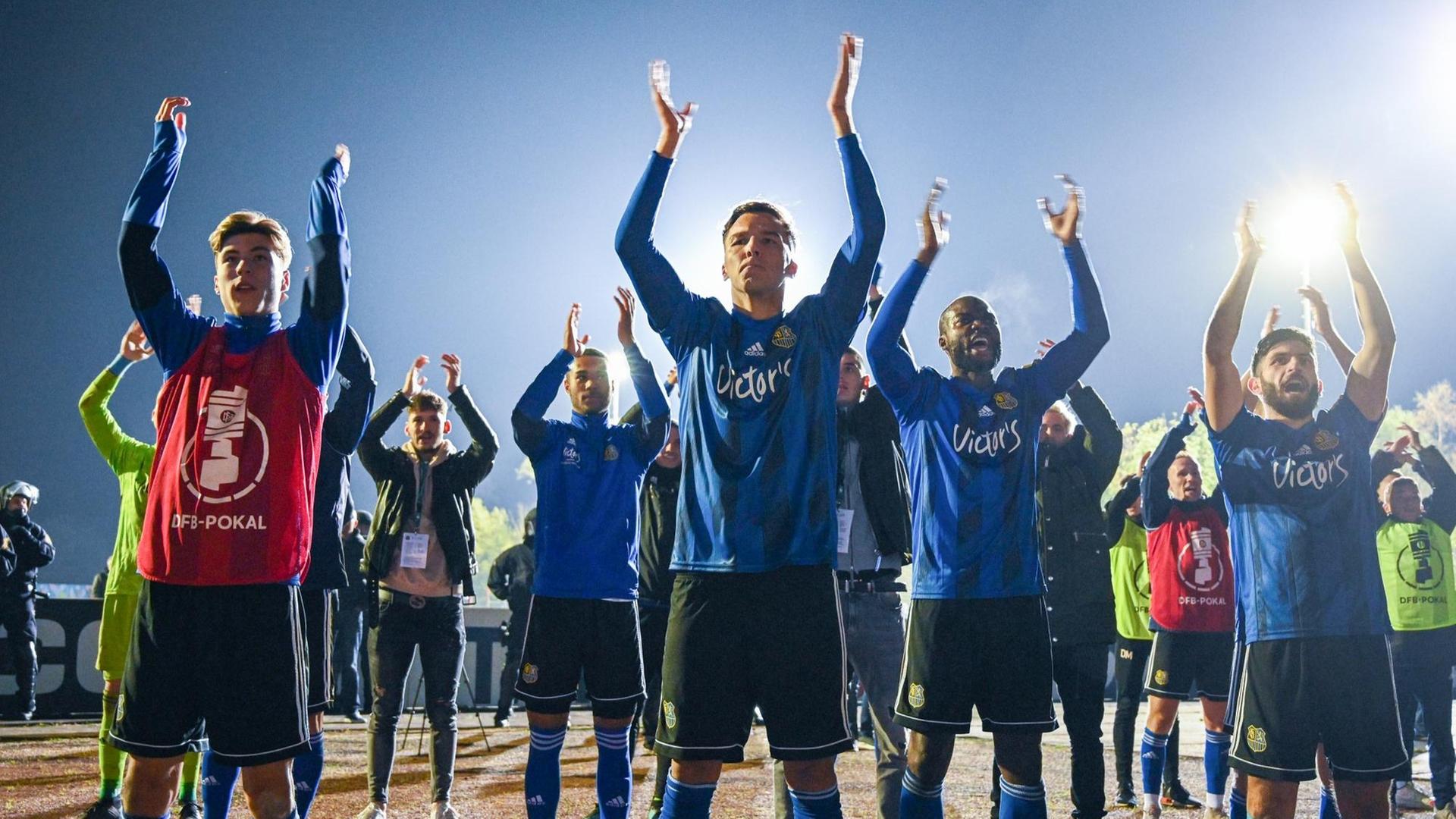 Die Spieler stehen in der Fan-Kurve und reißen die Arme hoch. Die Spieler stehen in der Fan-Kurve und reißen die Arme hoch.
