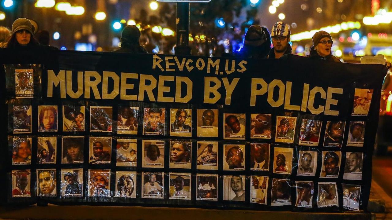 Demonstranten in Chicago halten ein Banner mit Fotos von Schwarzen hoch, auf dem steht "Ermordet durch die Polizei" Demonstranten in Chicago halten ein Banner mit Fotos von Schwarzen hoch, auf dem steht "Ermordet durch die Polizei"