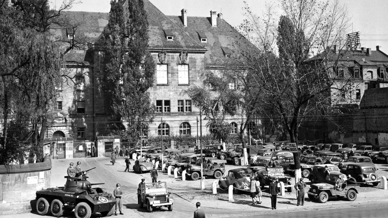 Schwarz-Weiß-Bild des Gerichtsgebäudes von außen. Davor stehen amerikanische Soldaten mit Jeeps und einem gepanzerten Fahrzeug. Schwarz-Weiß-Bild des Gerichtsgebäudes von außen. Davor stehen amerikanische Soldaten mit Jeeps und einem gepanzerten Fahrzeug.