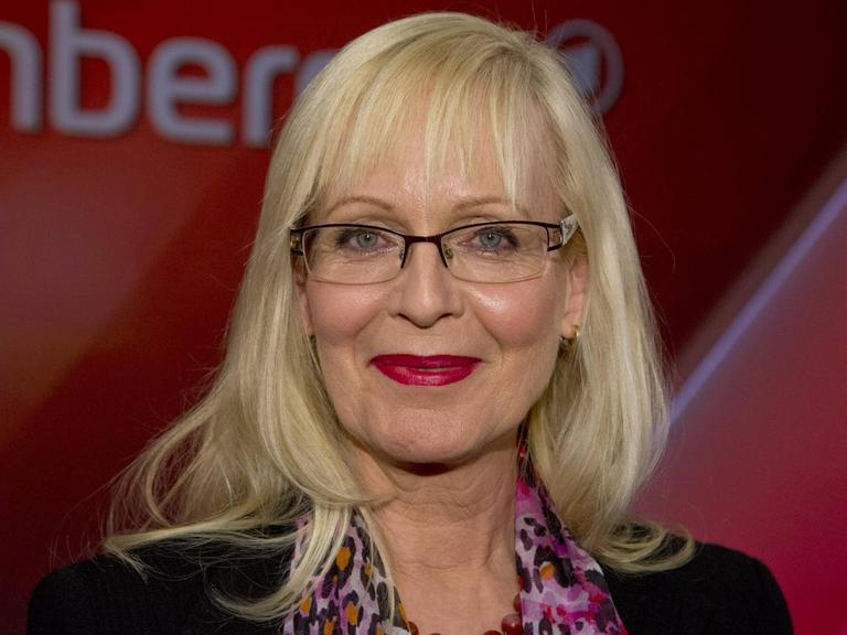 Susanne Schröter guckt vor einem dunkelroten Hintergrund lächelnd in die Kamera.