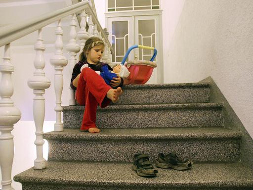Ein Mädchen sitzt im Treppenhaus und spielt mit einer Puppe.