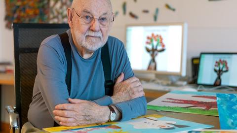 Eric Carle, Autor und Illustrator von "Die kleine Raupe Nimmersatt" sitzt an seinem Schreibtisch und schaut in die Kamera.
