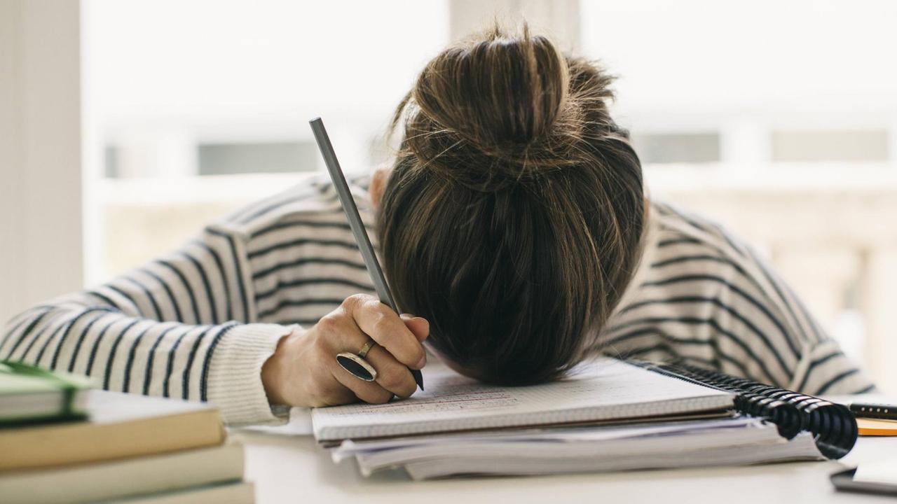 Eine Studentin liegt mit Ihrem Kopf auf einem Arbeitsheft. Eine Studentin liegt mit Ihrem Kopf auf einem Arbeitsheft.