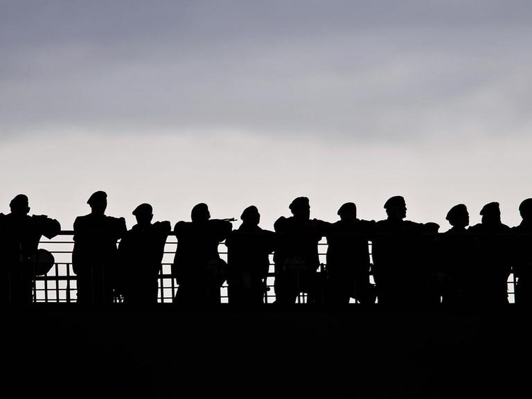Silhouette einer Gruppe von Polizisten, die sich an ein Geländer lehnen.