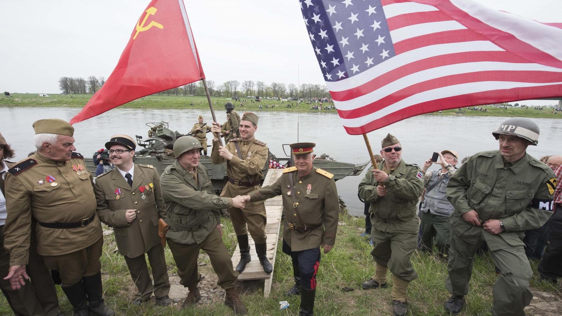 Darsteller amerikanischer und sowjetischer Soldaten reichen sich vor der Elbe die Hand. Darsteller amerikanischer und sowjetischer Soldaten reichen sich vor der Elbe die Hand.