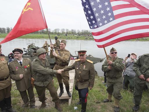 Darsteller amerikanischer und sowjetischer Soldaten reichen sich vor der Elbe die Hand.