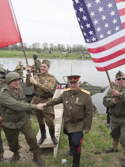 Darsteller amerikanischer und sowjetischer Soldaten reichen sich vor der Elbe die Hand.