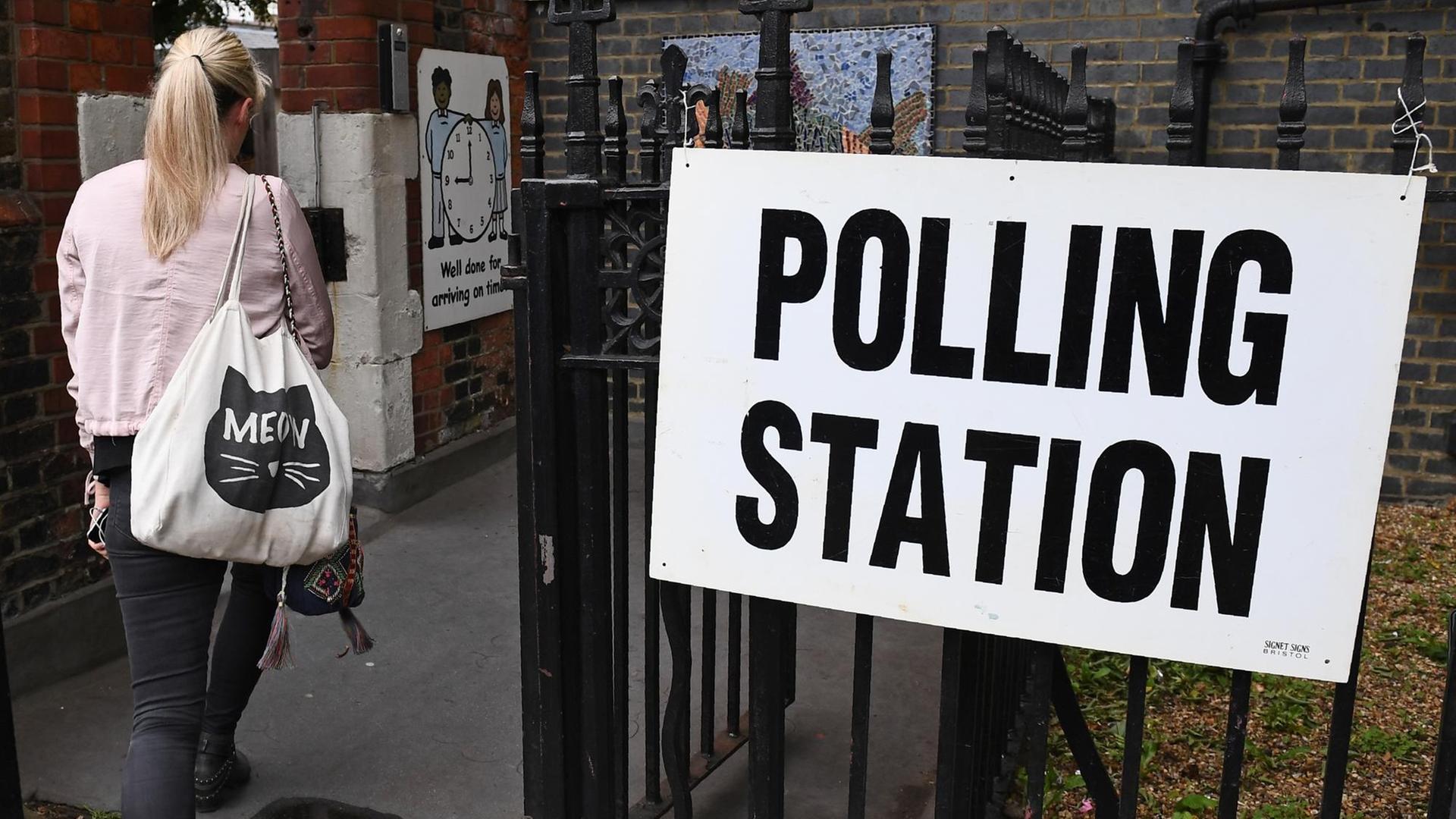 Eine Frau betritt ein Wahllokal in London. An der Seite hängt ein Schild mit der Aufschrift "Polling Station". Eine Frau betritt ein Wahllokal in London. An der Seite hängt ein Schild mit der Aufschrift "Polling Station".