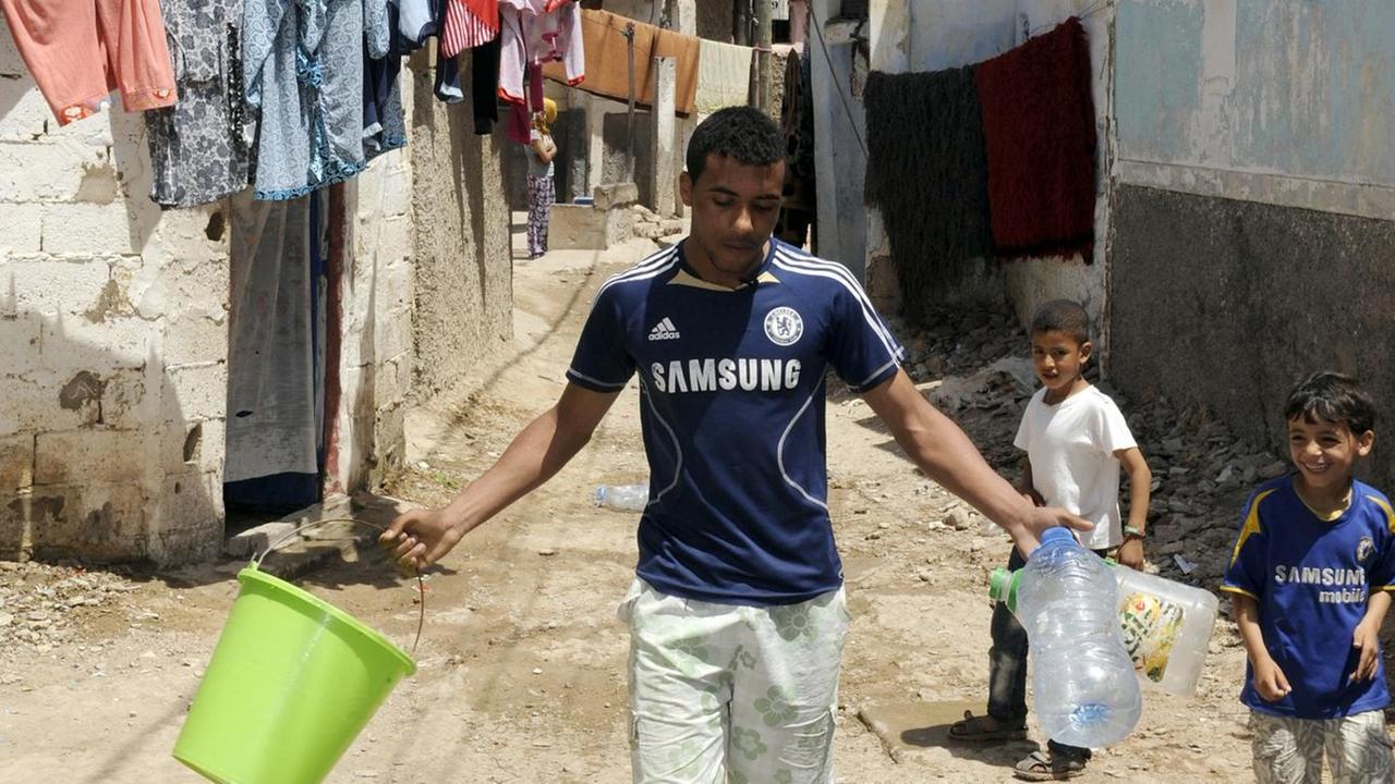 Ein Bewohner des marokkanischen Elendsviertels Sidi Moumen läuft mit Behältern an zwei Kindern vorbei.