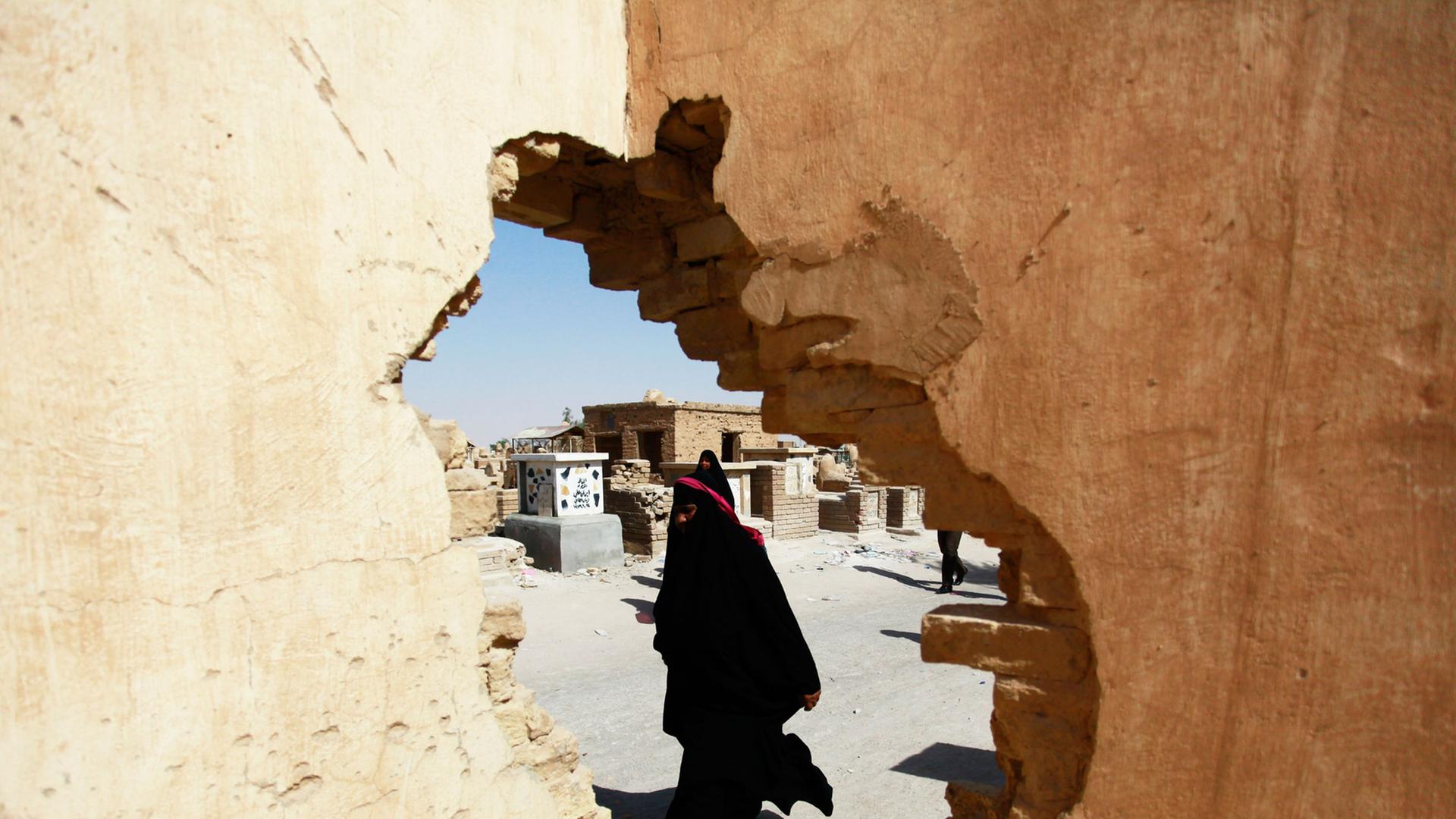 Ein Foto durch ein Loch in einer Mauer zeigt eine schiitische Irakerin, die an Gräbern auf einem der weltgrößten Friedhöfe in der Stadt Najaf vorbeiläuft. Ein Foto durch ein Loch in einer Mauer zeigt eine schiitische Irakerin, die an Gräbern auf einem der weltgrößten Friedhöfe in der Stadt Najaf vorbeiläuft.