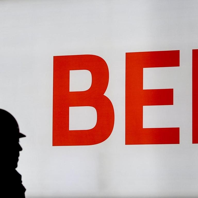 Ein Arbeiter geht vor dem Schriftzug vom Hauptstadflughafen Berlin Brandenburg Willy Brandt (BER) entlang