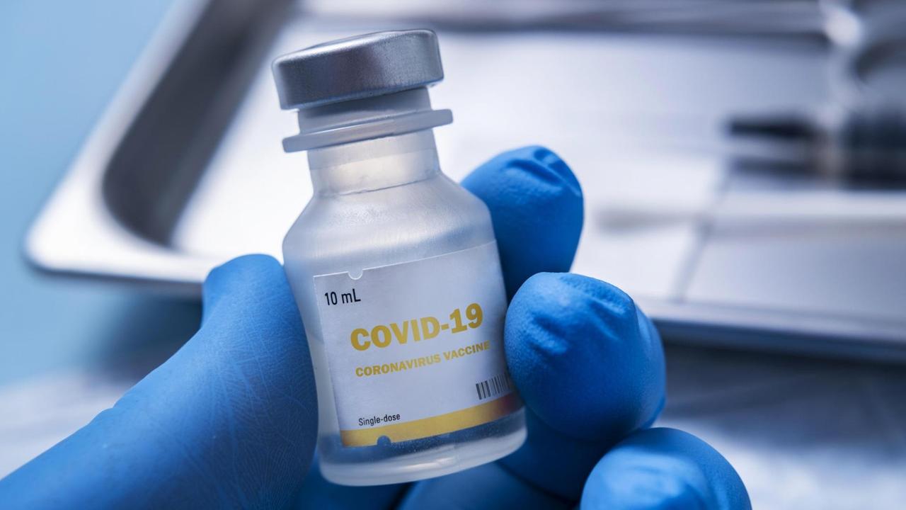 Nahaufnahme einer behandschuhten Hand, die ein Fläschchen mit der Aufschrift "Covid-19 - Coronavirus Vaccine" hält Nahaufnahme einer behandschuhten Hand, die ein Fläschchen mit der Aufschrift "Covid-19 - Coronavirus Vaccine" hält