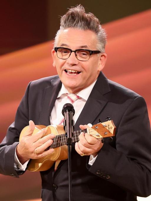 Der Entertainer Götz Alsmann spielt auf einer Bühne Ukulele.